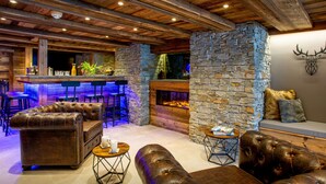 A rustic interior with a stone fireplace, leather seating, and a bar area with stools. - Chalet Colombine - luxury base 15p indoor pool & spa, cinema - OVO Network (Thônes)