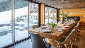 A dining area with a long wooden table set for a meal, large windows offering a view of a snowy landscape, and a wooden ceiling. - Chalet Colombine - luxury base 15p indoor pool & spa, cinema - OVO Network (Thônes)