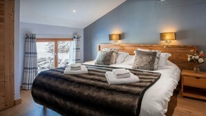 A bedroom with a large bed, two bedside lamps, a wooden headboard, and a view of a snowy landscape through a glass door. - Chalet Colombine - luxury base 15p indoor pool & spa, cinema - OVO Network (Thônes)