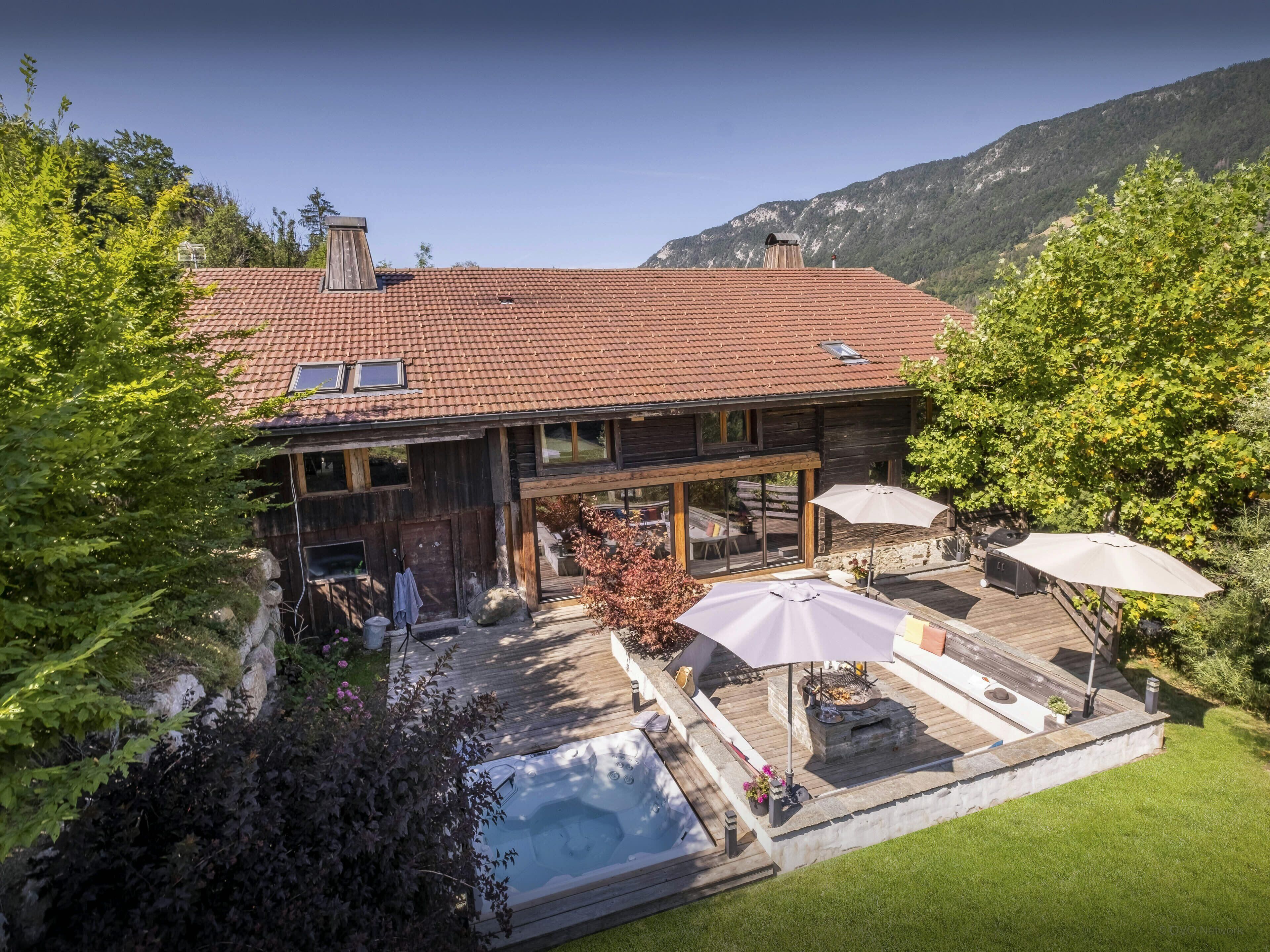 Une maison en bois avec un toit en tuiles, une piscine, un espace salon extérieur et une vue sur les montagnes en toile de fond.