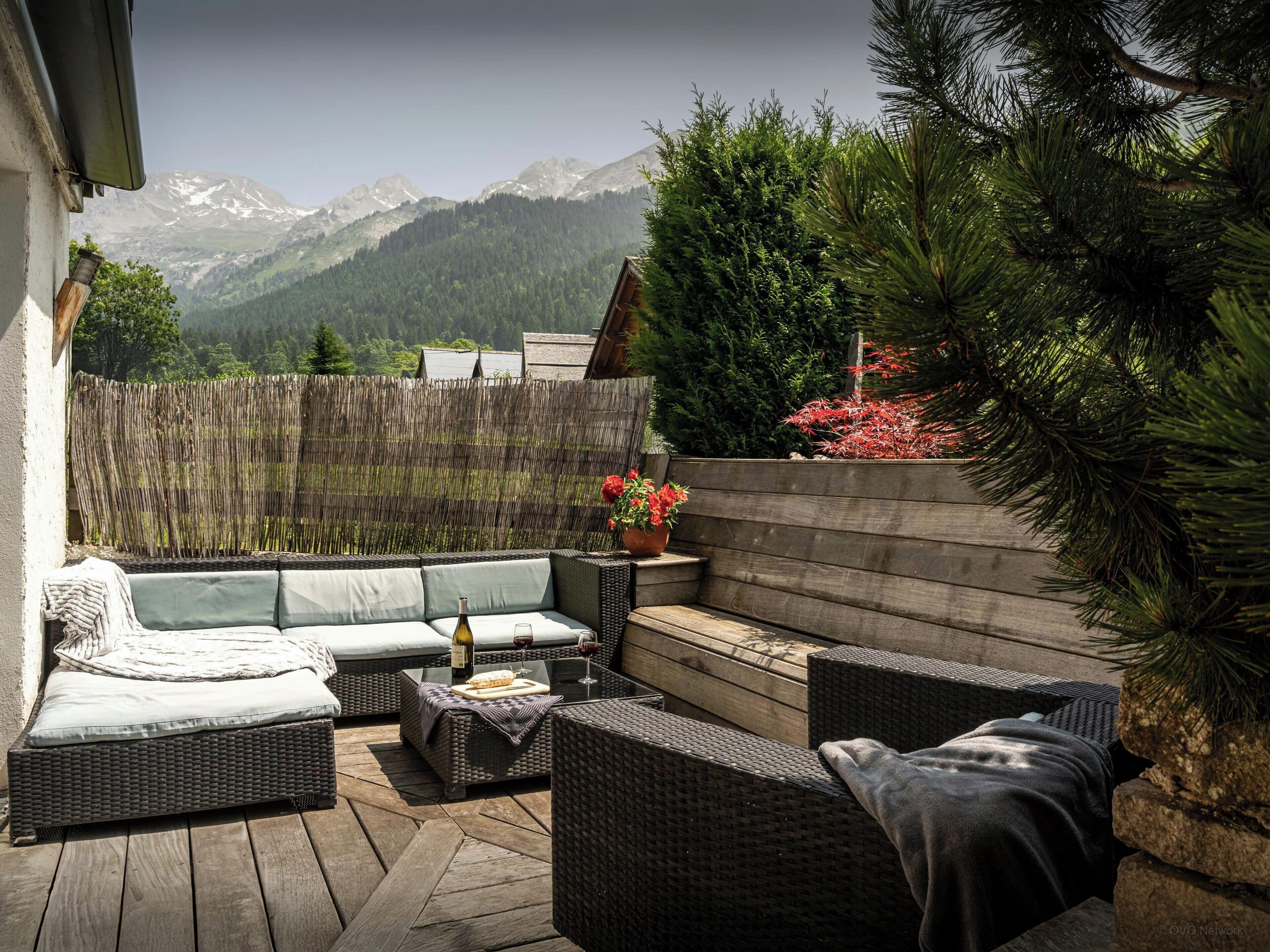 Un patio con muebles de mimbre, una mesa de madera y vistas a montañas.