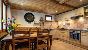 A wooden dining table with chairs, a vase of flowers, and a wall clock. - Chalet Le Petit Mazot - romantic break for 4 close to slopes - OVO Network (La Clusaz)