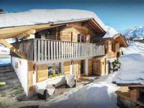 Un chalet en bois doté d’un balcon, d’un escalier en pierre et surplombant un paysage enneigé.