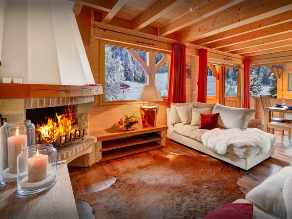 A cozy cabin interior with a fireplace, a sofa, a dining table, and a view of snowy trees. - Chalet des Enfants - ski-in ski-out base for 10, spa & views - OVO Network (La Clusaz)
