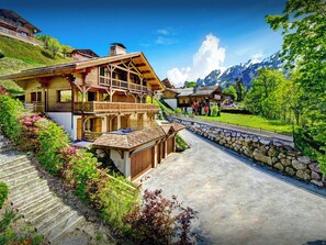 A traditional chalet with a wooden exterior, a stone staircase, and a view of a mountain range. - Chalet des Enfants - ski-in ski-out base for 10, spa & views - OVO Network (La Clusaz)