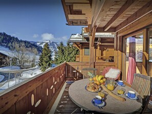 A wooden deck with a round table set for breakfast, overlooking a snowy mountain landscape. - Chalet des Enfants - ski-in ski-out base for 10, spa & views - OVO Network (La Clusaz)