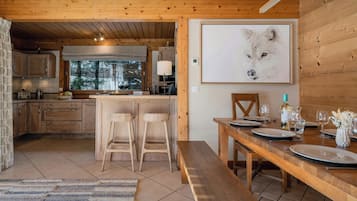 Interior de una cabaña de madera con cocina, comedor y un gran retrato enmarcado de un animal.