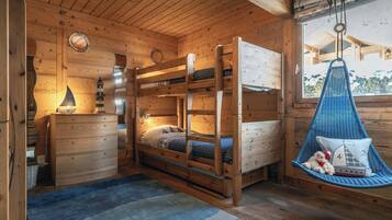 A wooden cabin interior with bunk beds, a desk, a hanging chair, and a window with a view.