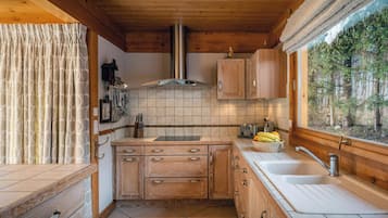 A compact kitchen with wooden cabinets, a stainless steel range hood, a window with a view of trees, and a sink with a faucet.