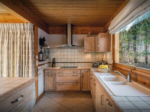 Una cocina compacta con armarios de madera, una campana extractora de acero inoxidable, una ventana con vistas a árboles y un lavamanos con grifo.
