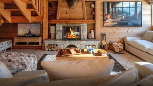 A cozy cabin interior with a stone fireplace, wooden staircase, and a large window with a mountain view. - Chalet J'Elage - family base 10p, open fire & mountain views - OVO Network (St Jean de Sixt)