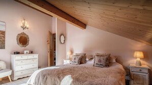 A cozy bedroom with a wooden ceiling, a bed with a fluffy blanket, a dresser, a nightstand with a lamp, and a mirror on the wall. - Chalet J'Elage - family base 10p, open fire & mountain views - OVO Network (St Jean de Sixt)