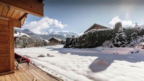 A wooden deck with a wicker chair and cushions, overlooking a snowy landscape with mountains and houses. - Chalet J'Elage - family base 10p, open fire & mountain views - OVO Network (St Jean de Sixt)