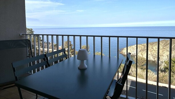 En balkon med bord og stole, der kigger ud over kysten.