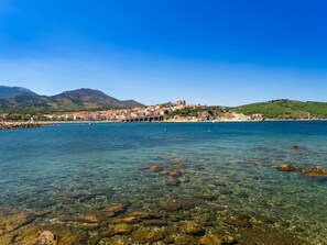 Un pueblo costero con aguas cristalinas, costa rocosa y un edificio destacado en una colina.