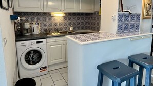Una cocina compacta con lavadora, un lavamanos y una pequeña zona de bar con taburetes.