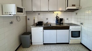 A compact kitchen with white cabinets, a microwave, a coffee maker, and a stove.