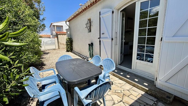 An outdoor patio with a table and chairs, a white door, and a view of a neighboring building.