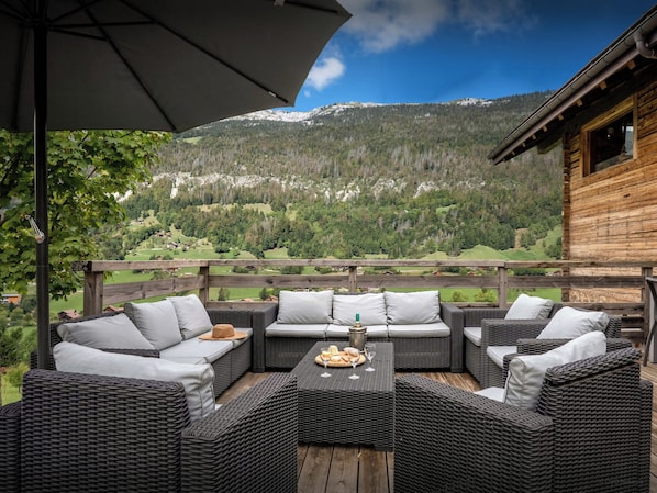 A wooden deck with wicker furniture and a table set with bread and wine glasses.