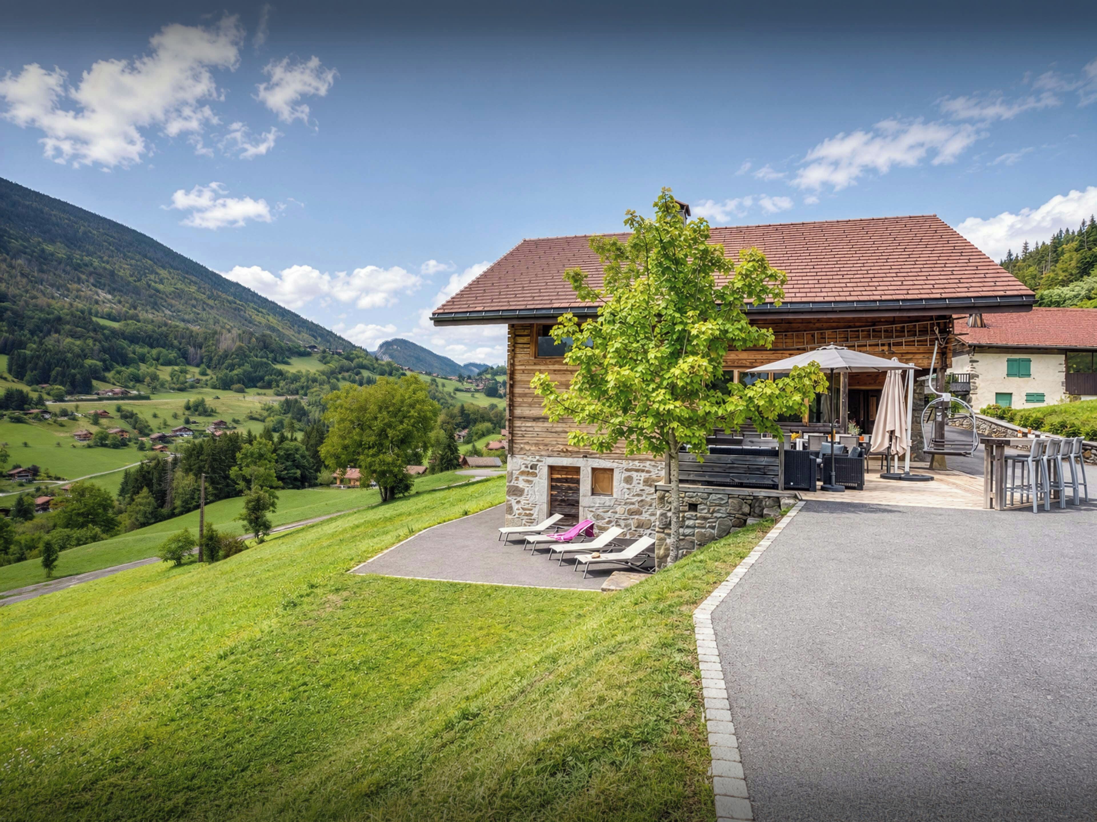 Un chalet doté d’une façade en pierre, d’un espace extérieur aménagé et offrant une vue sur un paysage montagneux.