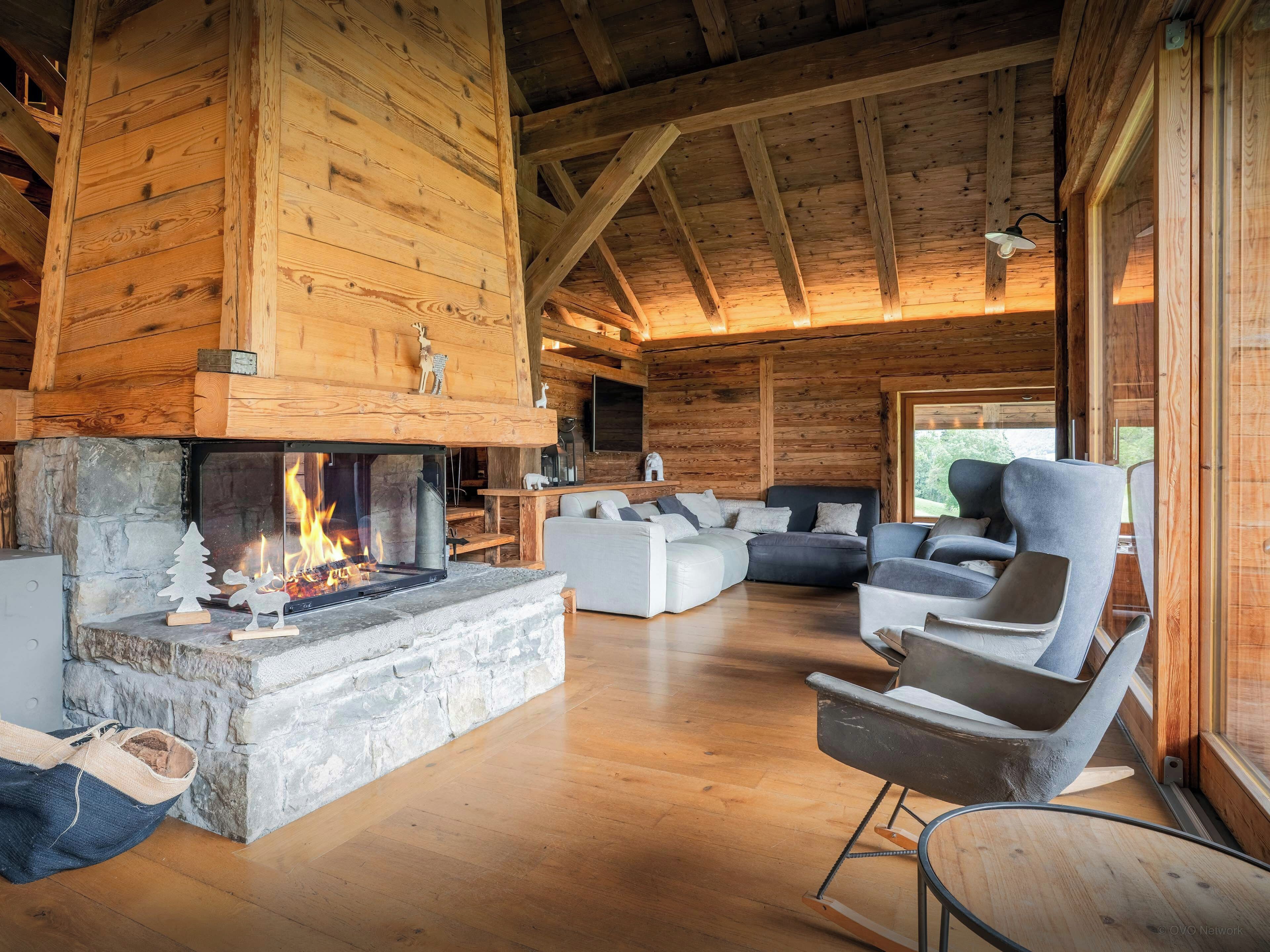 A log cabin interior with a stone fireplace, wooden ceiling beams, and modern furniture.