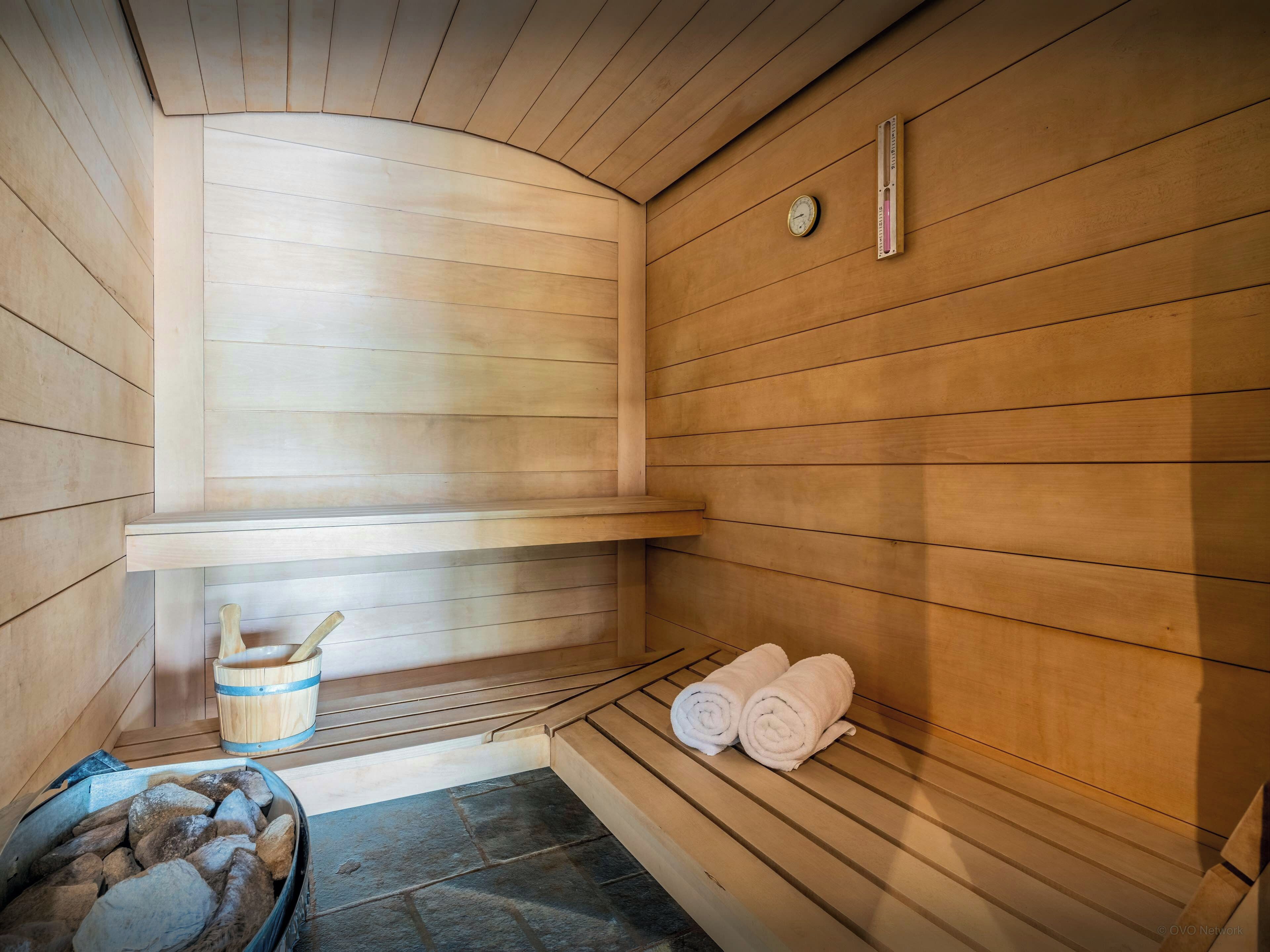 A sauna room with wooden walls, a bench, a bucket, and towels.