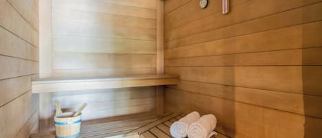 Una sala de sauna con paredes de madera, un banco, un balde y toallas.