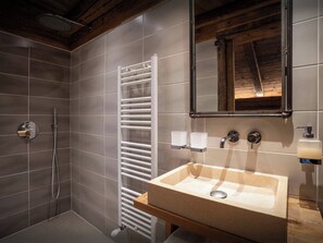 Un baño con ducha, toallero blanco, tocador de madera con lavabo y espejo.
