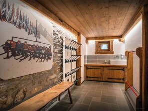 Un intérieur rustique avec un banc en bois, une fresque murale sur le thème du ski, un mur en pierre et un coin cuisine doté de meubles en bois et d’un évier.