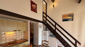 A compact kitchen with a dining area, a staircase, and a refrigerator. - House 2 rooms, cabin, 6 pers, 400m from beach, parking, terrace (Port-la-Nouvelle)