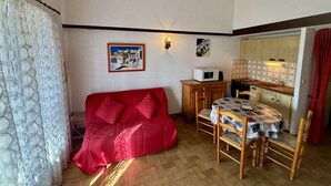 A compact living space with a red sofa, a dining table with chairs, a kitchenette, and a painting on the wall. - House 2 rooms, cabin, 6 pers, 400m from beach, parking, terrace (Port-la-Nouvelle)