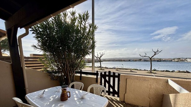 A covered outdoor seating area with a table and chairs, overlooking a body of water and a distant shoreline. - House 2 rooms, cabin, 6 pers, 400m from beach, parking, terrace (Port-la-Nouvelle)