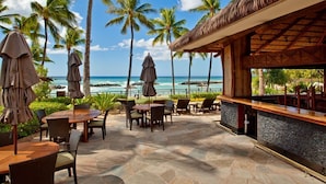 A beachfront patio with tables and chairs, a bar area, and palm trees.