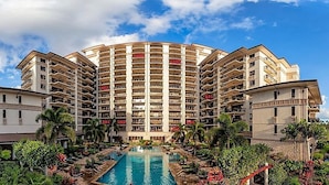A multi-story hotel with a central pool surrounded by lush greenery.