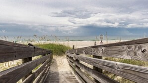A wooden boardwalk leading to a beach with a sign indicating a tide warning.