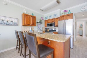 Cocina con armarios de madera, encimera de granito, refrigerador de acero inoxidable y zona de bar con sillas.