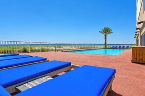 A poolside area with blue lounge chairs, a palm tree, and a view of the ocean.