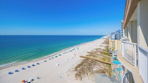 A beach view from a balcony with a clear sky, a sandy beach with umbrellas, and a pool area. - Royal Palms 144 Beachfront Gulf Escape  Pool, Hot Tub & Sauna (Gulf Shores)