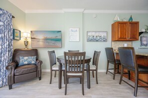 Un comedor con una mesa redonda, cuatro sillas, un sillón de cuero marrón, una lámpara y detalles decorativos en la pared.