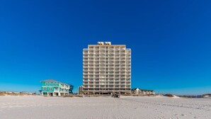 A tall hotel with multiple balconies, a beach in the foreground, and a clear blue sky. - Royal Palms 144 Beachfront Gulf Escape  Pool, Hot Tub & Sauna (Gulf Shores)