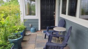 Eine überdachte Terrasse mit Steinböden, einer schwarzen Tür und blauer Gartenmöbel.