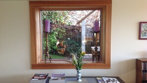 Ein Zimmer mit Fensterblick auf einen Garten, ein Tisch mit Zeitschriften und eine Vase mit Blumen.