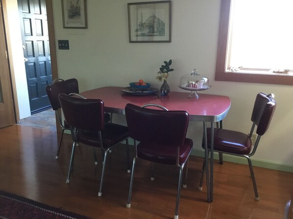 A dining area with a red table, four dark chairs, a vase with flowers, and a cake stand with pastries.