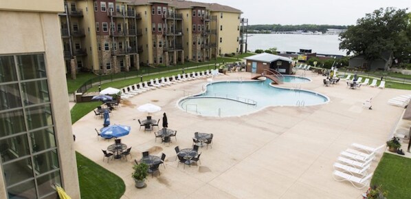 A pool area with lounge chairs and tables, surrounded by a building with multiple balconies.