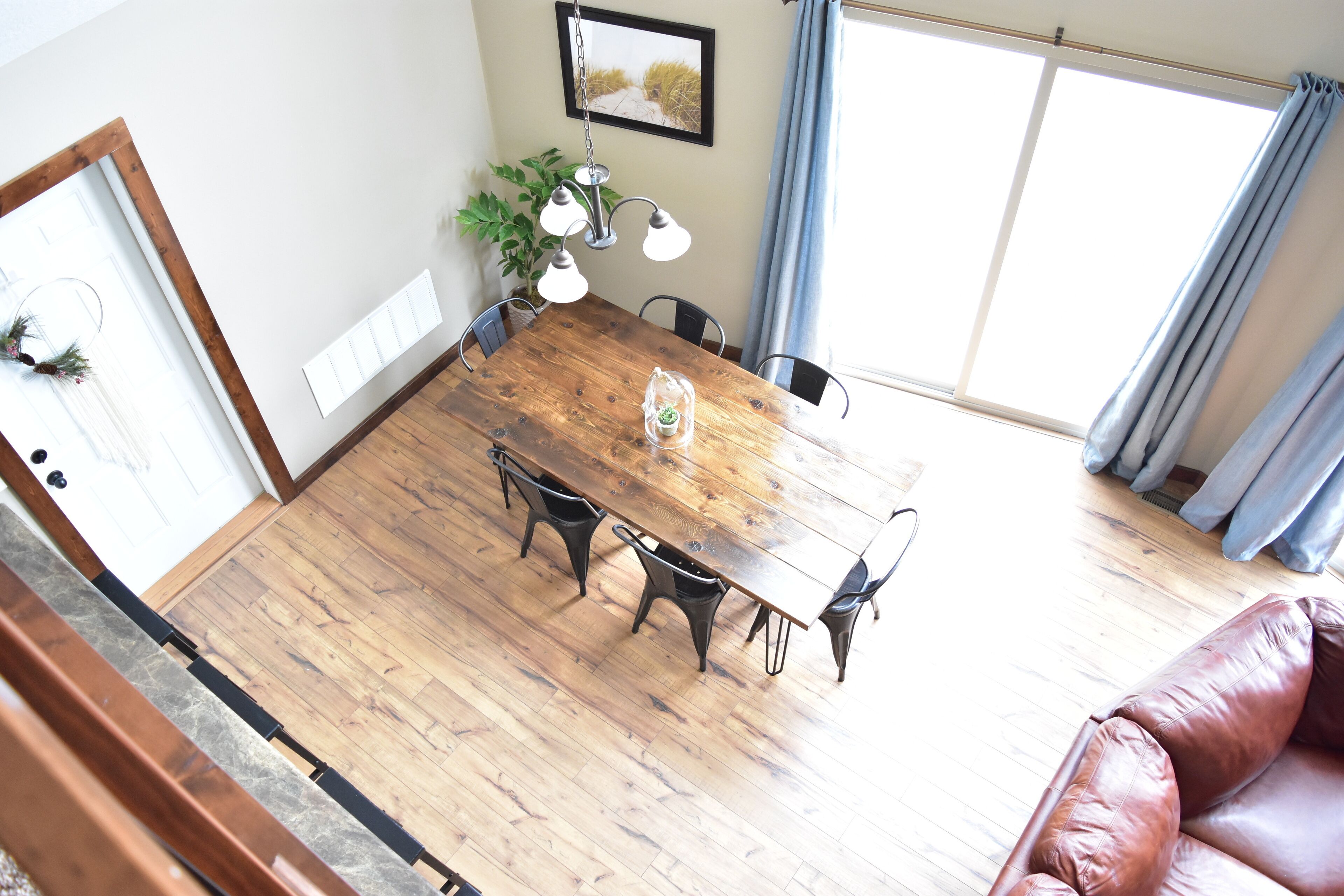 Un comedor con una mesa de madera, cuatro sillas, una planta en maceta y una lámpara colgante.