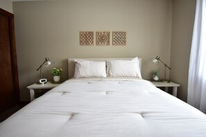 Un lit bien fait, avec du linge de lit blanc, deux tables de chevet avec des lampes et trois panneaux décoratifs fixés au mur.