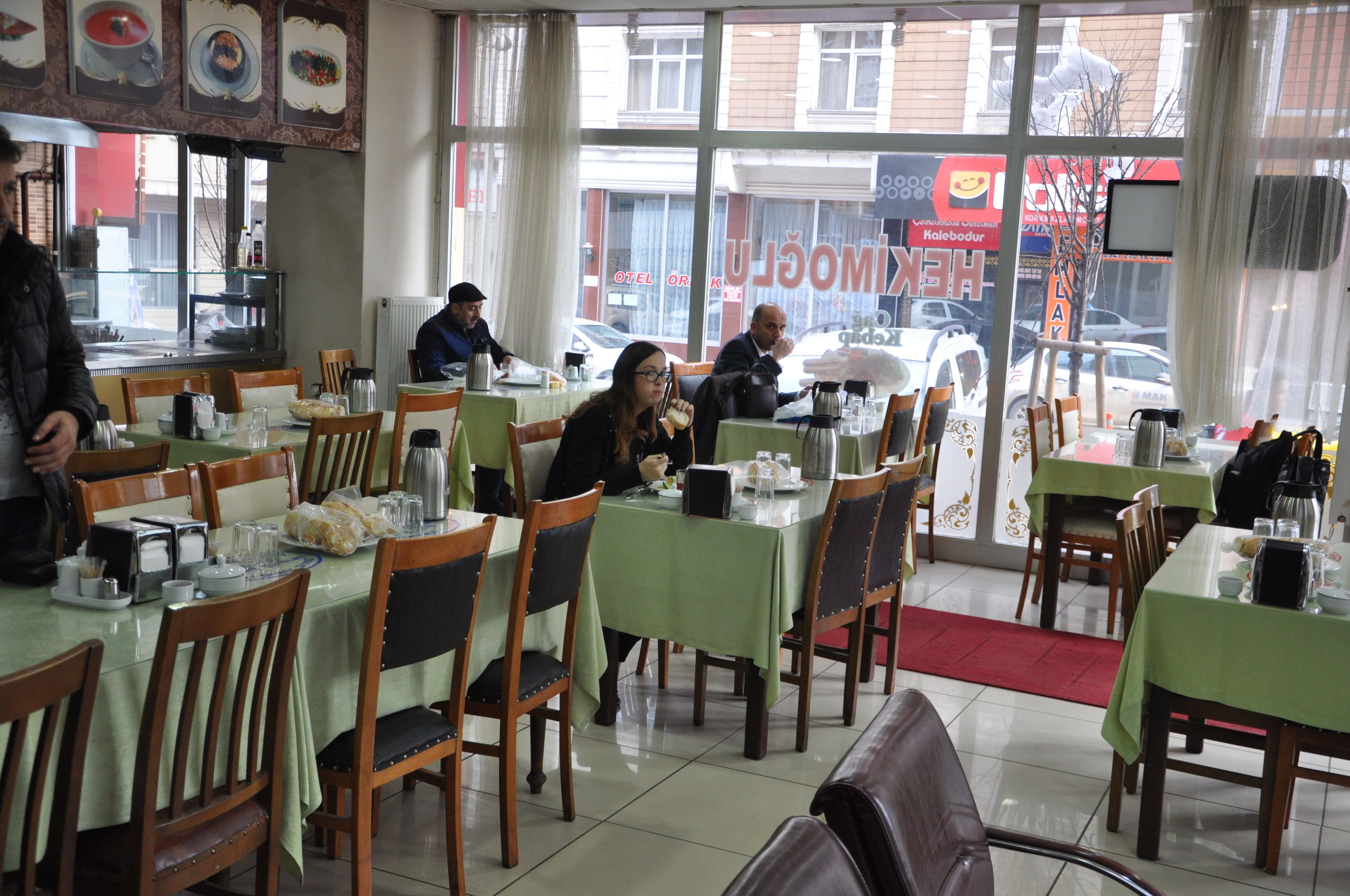 Un restaurant amb diverses taules i caires, finestres amples i vistes al carrer.