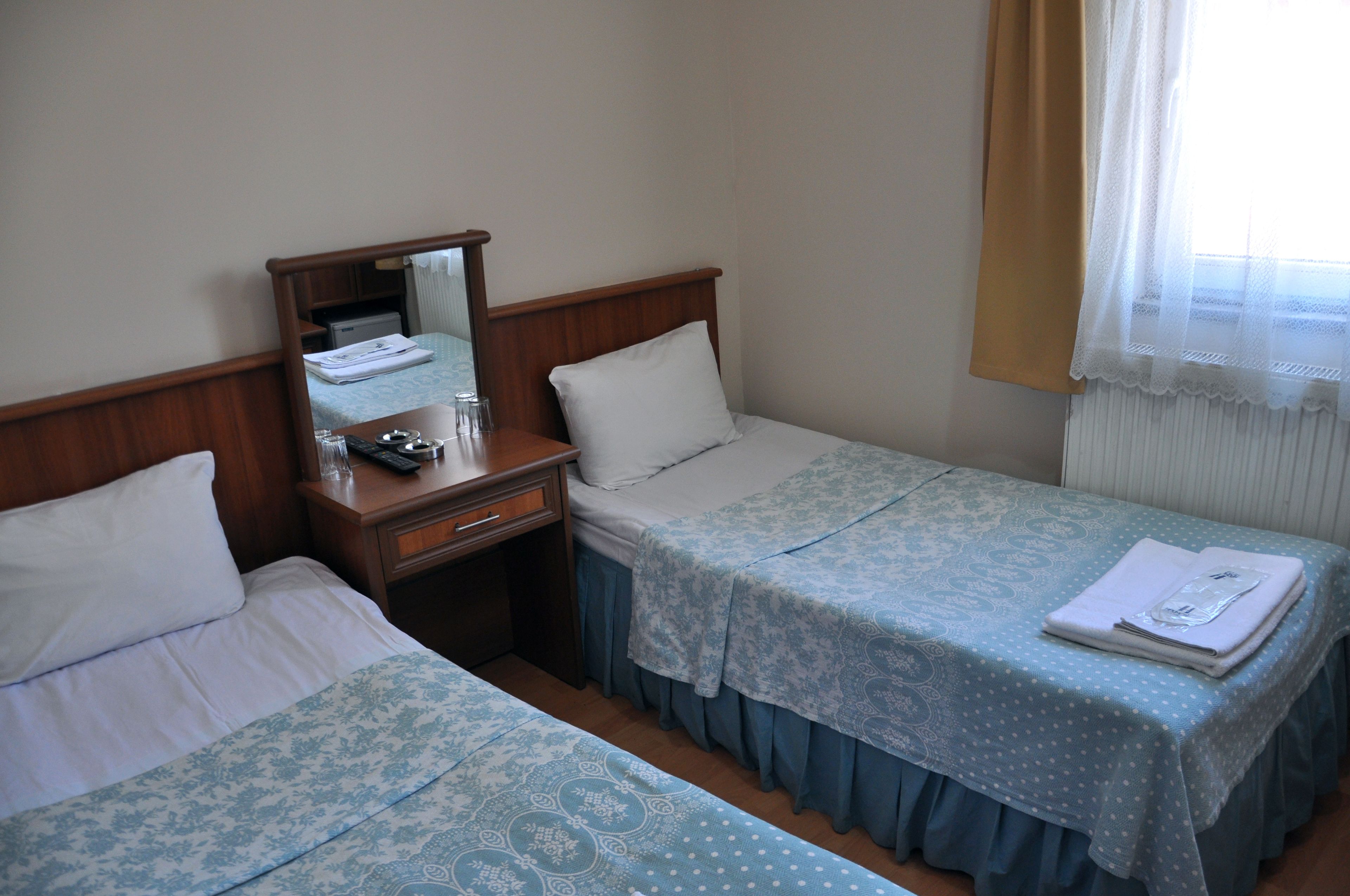 A hotel room with two beds, a bedside table, a mirror, and a window with curtains.