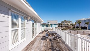 A wooden deck with a white railing, a picnic table, and a pool in the background.
