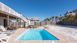 A swimming pool with lounge chairs, a wooden deck, and a sandy beach area.